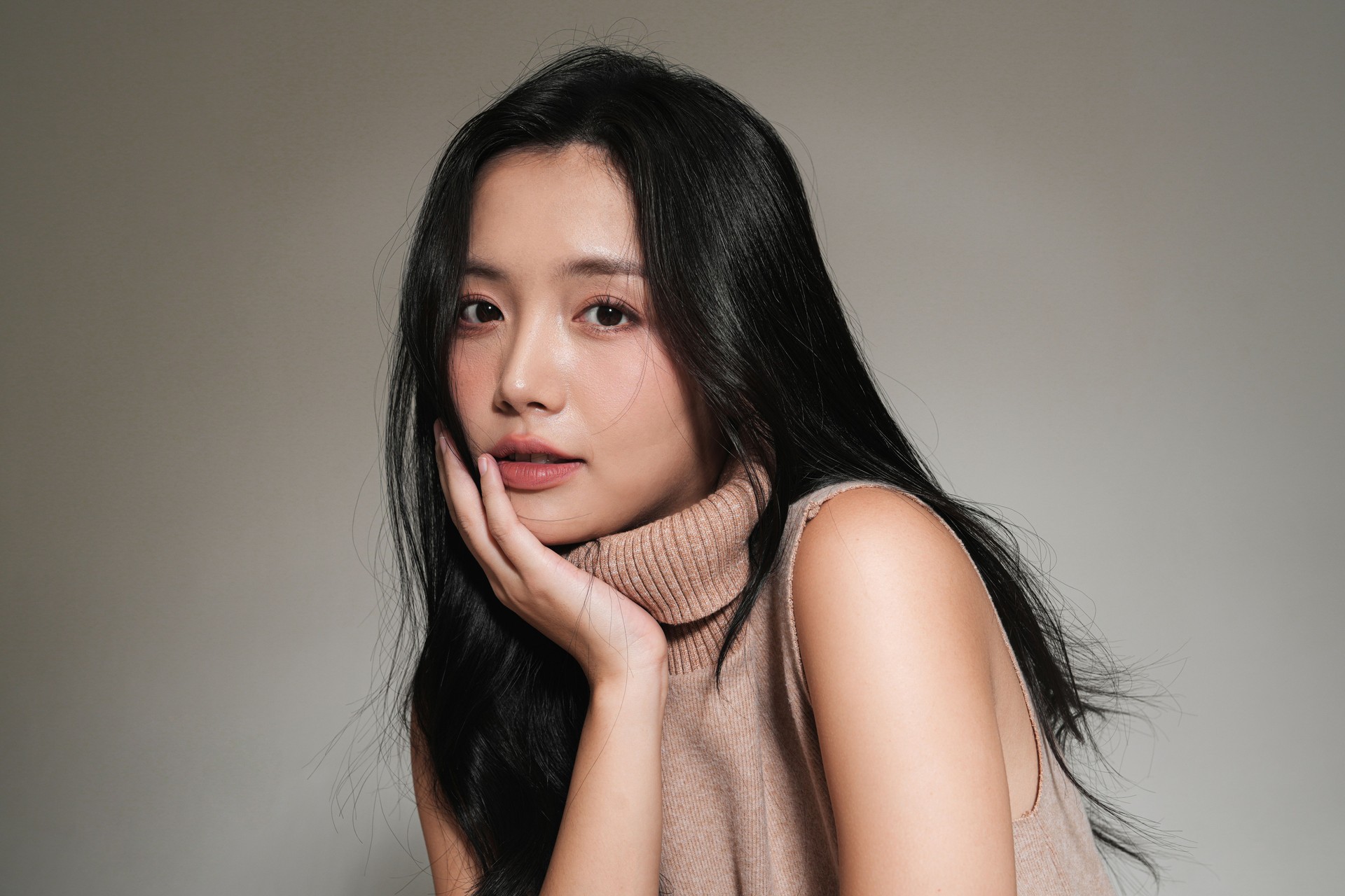 Stylish portrait of young woman in sweater shot against gray background